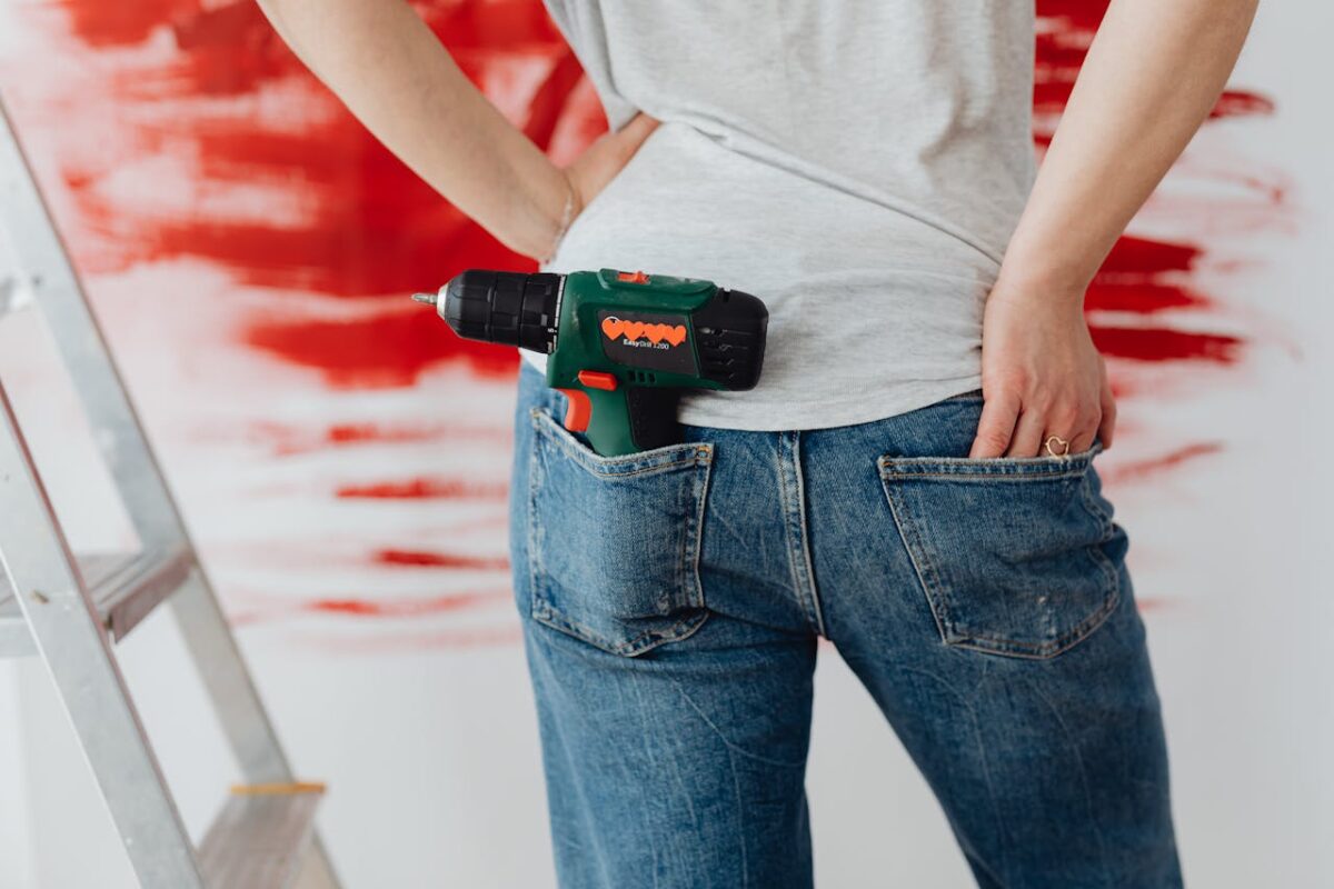 Woman holding electric drill in back pocket with red paint background.